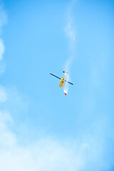 Smoke, water and helicopter in sky for emergency, disaster management and firefighter service. Fire, damage control and chopper in flight with bucket, spray or rescue volunteer in nature conservation