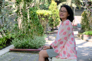 Naklejka premium A woman sitting on a concrete bench is looking at one side smiling, her hands on her lap