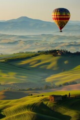 Fototapeta premium A hot air balloon drifting above rolling hills, with a softly blurred background of green fields and distant mountains. 