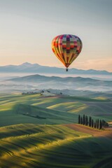 Obraz premium A hot air balloon drifting above rolling hills, with a softly blurred background of green fields and distant mountains. 