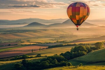 Fototapeta premium A hot air balloon drifting above rolling hills, with a softly blurred background of green fields and distant mountains. 