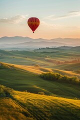 Fototapeta premium A hot air balloon drifting above rolling hills, with a softly blurred background of green fields and distant mountains. 