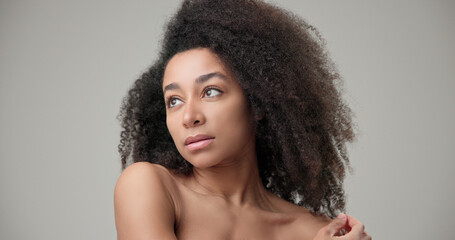 Beauty and healthcare concept - beautiful African American woman with curly afro hairstyle and clean, healthy skin touches her cheek and face with her hand, posing and looking at the camera