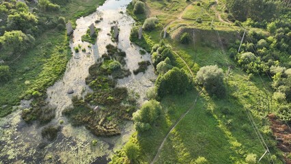 wild abandoned aerial top view country side landscape grass land lawn and swamp pond with bridge ruins column architecture objects