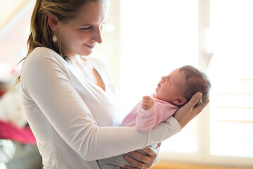 Mom holding newborn baby, looking at infant lovingly. Unconditional paternal love, Mother's Day...