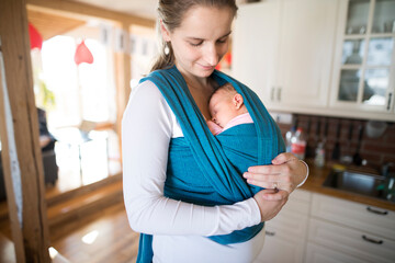 Mother holding small baby, carry her in baby sling, wrap around the house. Unconditional paternal...