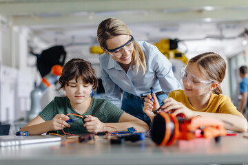 Female teacher helping to girls working on small robot, building robotic kit in after-school robotics club. Children learning robotics in Elementary school. Girls in science.