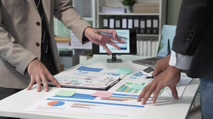 A collaborative meeting at an office desk focusing on teamwork, with discussions centered around financial charts and the sub-account management of work in process in production cost accounting. - Powered by Adobe