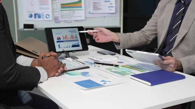 A collaborative meeting at an office desk focusing on teamwork, with discussions centered around financial charts and the sub-account management of work in process in production cost accounting.