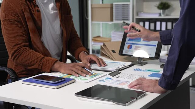 A collaborative meeting at an office desk focusing on teamwork, with discussions centered around financial charts and the sub-account management of work in process in production cost accounting.