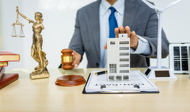 A male Asian lawyer in a formal suit works at his desk, focusing on contracts, legal matters, and urban planning issues such as building models, zoning, ordinances, and municipal regulations.