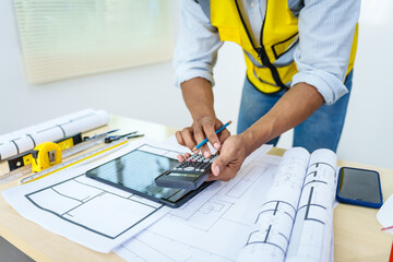 Asian male architect works at desk with house model toy and A3 paper blueprints, construction real estate law, zoning, permits, and resolving property disputes through arbitration and litigation.