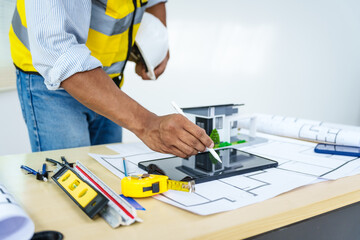 Asian male architect works at desk with house model toy and A3 paper blueprints, construction real estate law, zoning, permits, and resolving property disputes through arbitration and litigation.