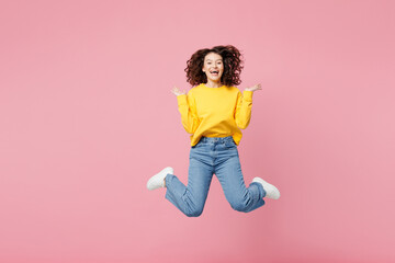 Full body young shocked surprised woman wearing yellow sweatshirt casual clothes jump high spread hands look camera isolated on plain pastel light pink background studio portrait. Lifestyle concept.