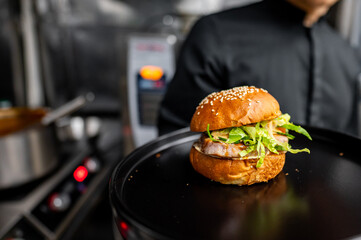 A freshly prepared burger with sesame bun, greens, and meat patty on a black plate