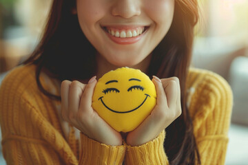 A smiling woman holds a happy face in her hand, symbolizing positive thinking and mental health awareness. This concept promotes the importance of mental health and World Mental Health Day.