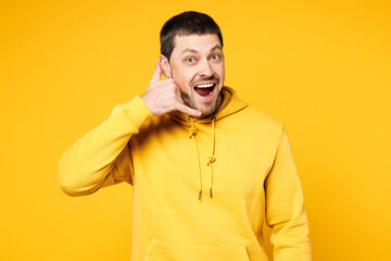 Young smiling happy cheerful fun Caucasian man he wears hoody casual clothes doing phone gesture like says call me back isolated on plain yellow orange background studio portrait. Lifestyle concept.