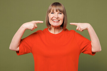 Elderly smiling blonde woman 50s years old wear orange t-shirt casual clothes point index finger on opened mouth and teeth isolated on plain pastel green background studio portrait. Lifestyle concept.