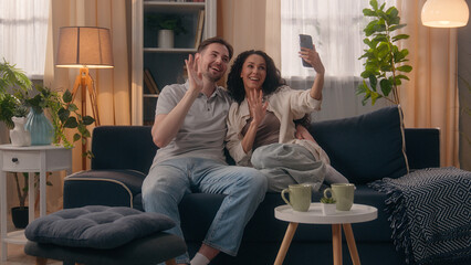 Obraz premium Happy family couple smiling talking influencers vloggers Caucasian man guy male husband boyfriend Hispanic Latino woman girl female wife girlfriend at home talk video call conference mobile phone app