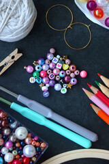 Colorful beads, coloring pencils, glitter, needles, string, hoop, tape and scissors on dark...