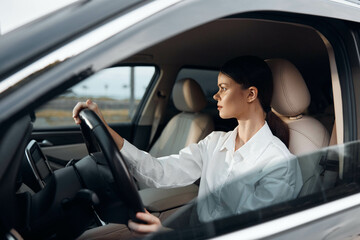 Woman, car, driver, steering wheel, looking at camera a woman is seated in the driver's seat of a car, hands on the steering wheel, and is gazing directly at the camera, conveying a sense of focus and