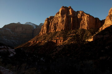 Sunset at Zion National Park - the setting sun is barely illuminating the peaks of the red rocks with snow sprinkled around