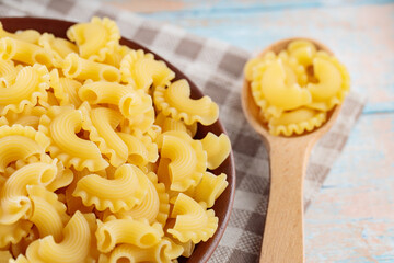 Bowl of Dry Italian Creste di Gallo Pasta with Wooden Spoon on Linen Napkin