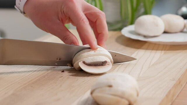 Close-up chef using a sharp knife slices champignon mushrooms, wooden board Preparation for salads, mini pizza with mushrooms, pie, appetizer, side view, macro