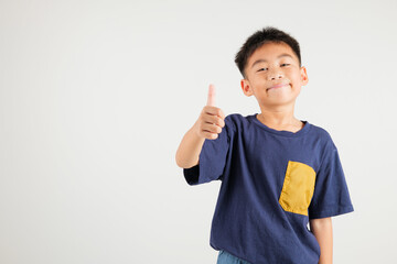 Confident Asian young boy in a studio portrait isolated on white background makes a thumbs up OK sign, symbolizing agreement and success. primary child smile radiates positivity and satisfaction