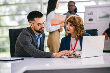 Obraz premium Two business people working together on laptops and tablets in office.