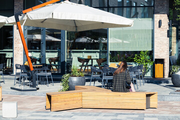 Naklejka premium summer hot temperature restaurant cafe patio furniture space umbrella tables and benches for rest and unrecognizable girl sitting back to camera