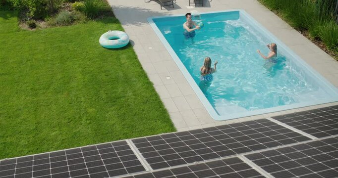 A cheerful family plays in the pool, in the foreground are solar power panels on the roof of their house