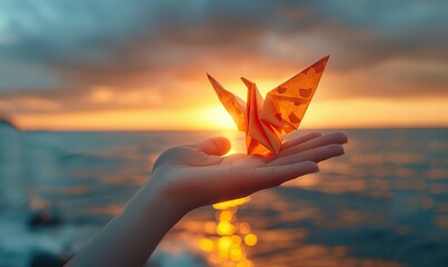 Child's hands holding a paper origami bird against a sunset sky, symbolizing freedom.