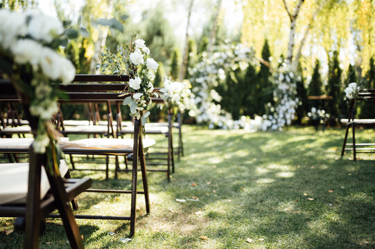 Wooden chairs decorated with flowers for an outdoor wedding ceremony