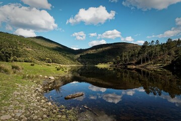 Scenic view of a lake surrounded by lush green hills and a clear blue sky with fluffy clouds