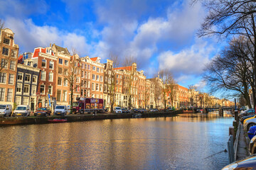 Cityscape on a sunny winter day - view of the houses and the city canal with boats in the historic center of Amsterdam, The Netherlands