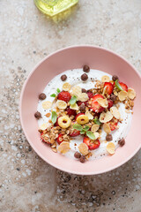 Yogurt bowl with fresh strawberry, granola and flakes, vertical shot on a beige granite background, high angle view