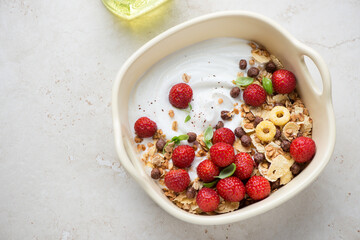 Greek yogurt with fresh strawberries, breakfast flakes and granola, horizontal shot on a light-beige stone background, high angle view