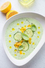 Chilled soup made of cucumber and topped with sweet corn, vertical shot on a white stone background, above view