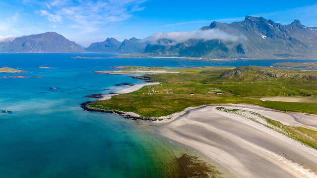 Kolbeinsanden Beach, Lofoten serene beach nestled within a dramatic fjord landscape in Norway. The azure waters and lush green hills create a stunning contrast against the towering mountains