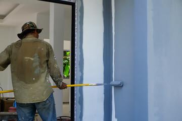 Asian mechanical painter man builder using brush to painting primer white color on concrete wall inside of house