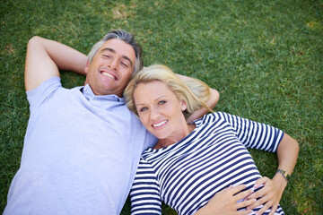 Fototapeta premium Relax, love and portrait of couple on grass in park for romantic outdoor date with bonding and connection. Happy, marriage and people laying on green lawn in garden, nature or field from high angle.