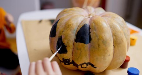 Close-up of a hand painting a jack-o'-lantern face on a pumpkin with black paint