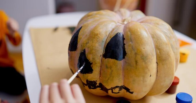 Close-up of a hand painting a jack-o'-lantern face on a pumpkin with black paint
