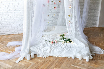 Bed with flowing curtains and garland flowers levitating, hanging flowers. Bedroom interior design.White Mattress for sleeping on the wooden floor with white linens in modern minimalist bright bedroom © stock_studio