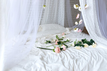 Roses on bed in room. Bedroom interior design. Closeup of bed with scattered pink and white roses. Bed with flowing curtains and garland flowers levitating, hanging flowers. Honeymoon. Valentine day © stock_studio