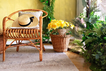 Fototapeta premium Concept Summer travel and vacation. Modern boho room with interior design, rattan chair and green plants in baskets. Wicker wooden chair with pillows and straw hat. Eco furniture, natural furniture. 
