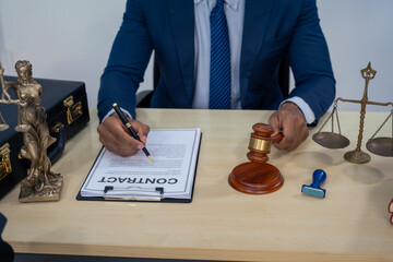 An Asian businessman in a formal suit works alone at a lawyer's desk, by golden scales, law books,...