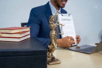 An Asian businessman in a formal suit works alone at a lawyer's desk, by golden scales, law books,...