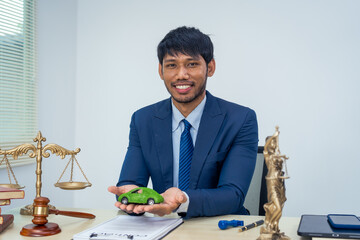 An Asian businessman in a formal suit works alone at a lawyer's desk, with golden scales, law...